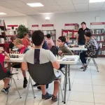 Adhésion au club l'échiquier Agenais, dans la bibliothèque d'une école des tables blanches sont disposées et des jeunes enfants jouent aux échecs surveillés par un animateur.